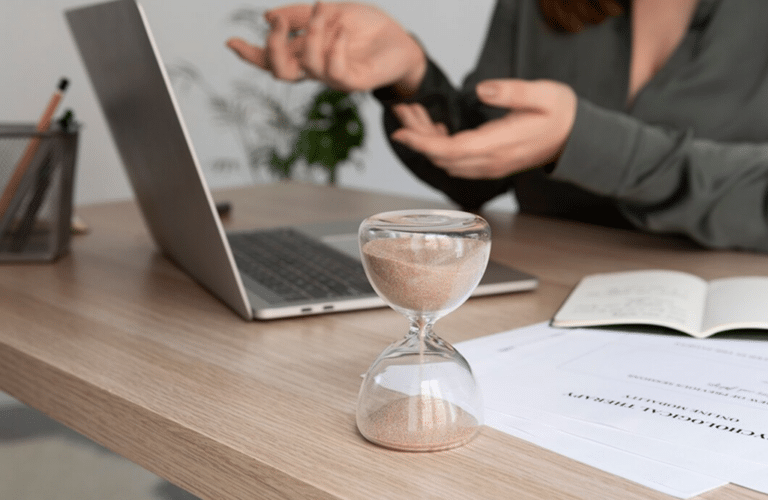 a hourglass on a table with a laptop and a person gesturing